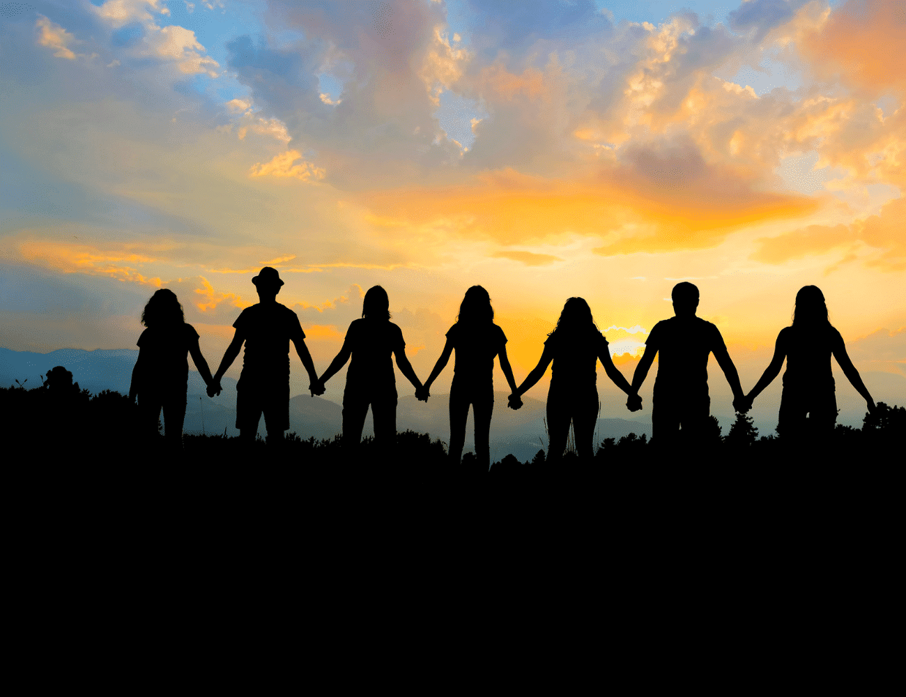 Group holding hands at sunset, silhouetted against a colorful sky.